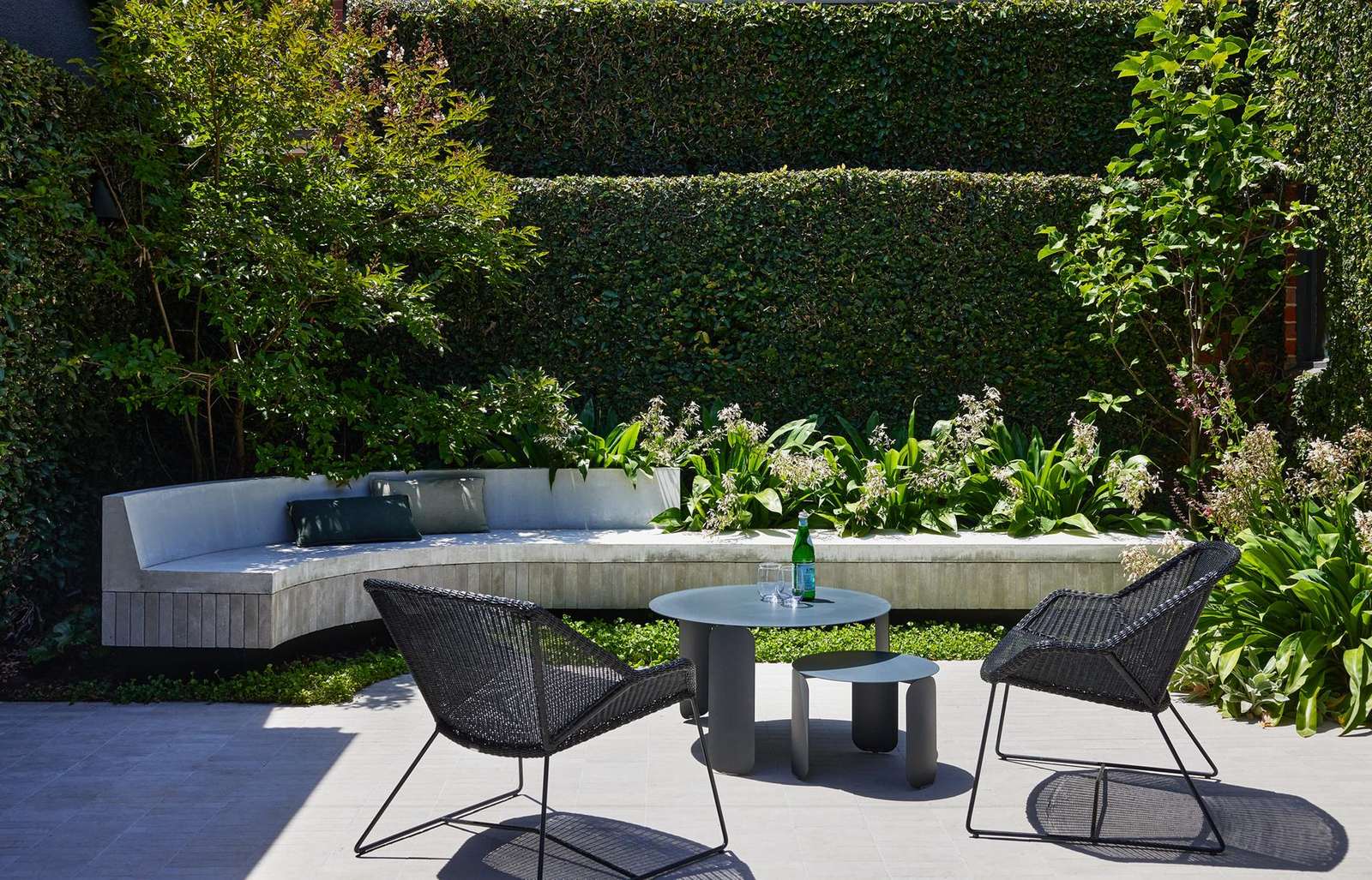 Curved concrete bench set against a clipped hedge in the Caulfield courtyard