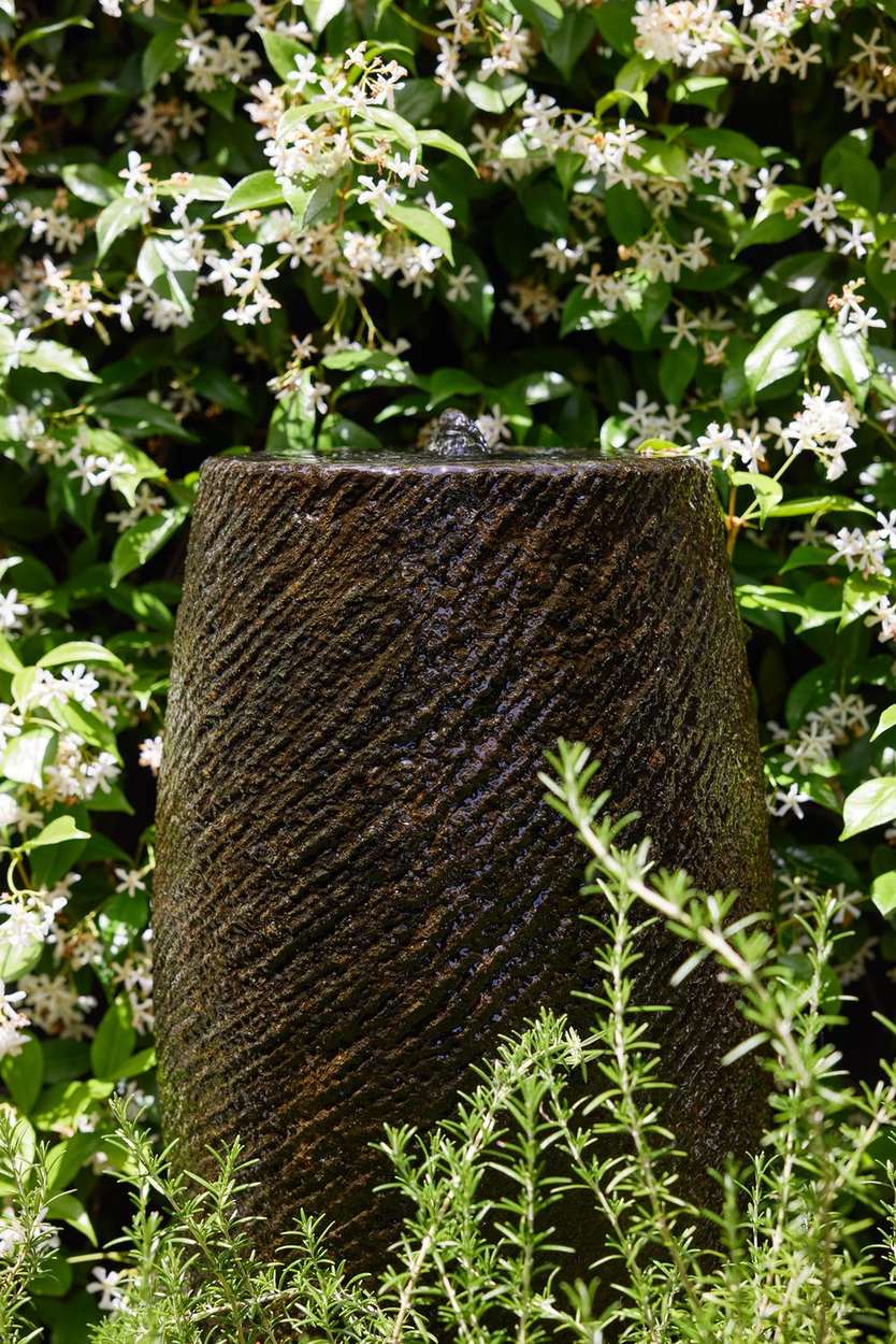 The stone water feature in close detail, water sheeting down the fluted face