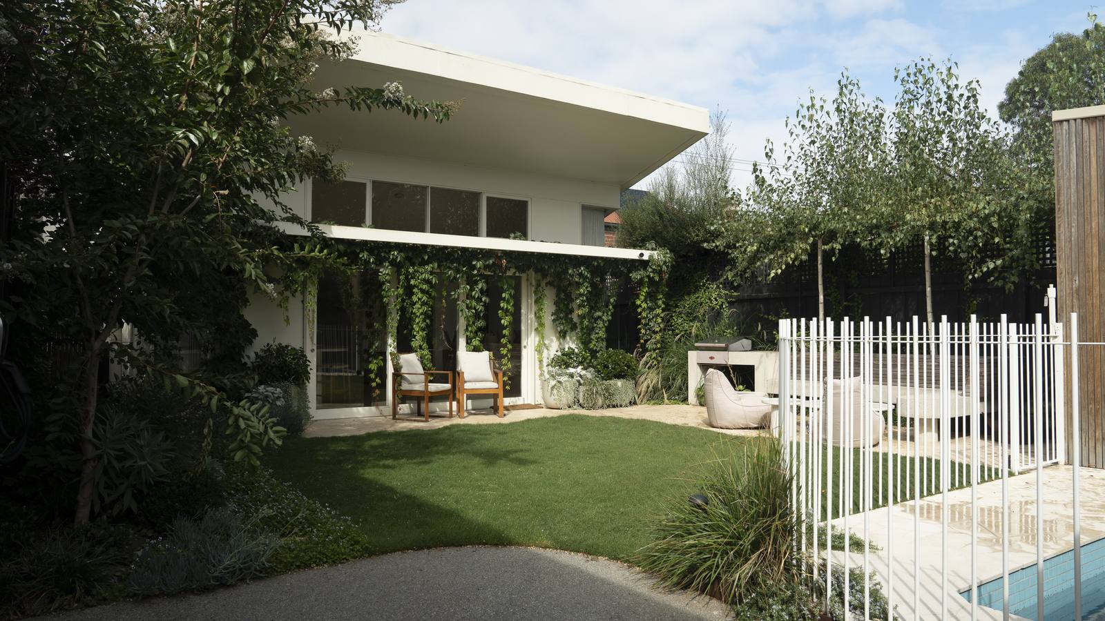 The rear garden at Clifton Hill, lawn running up to a white flat-roofed pavilion with the pool fence to one side