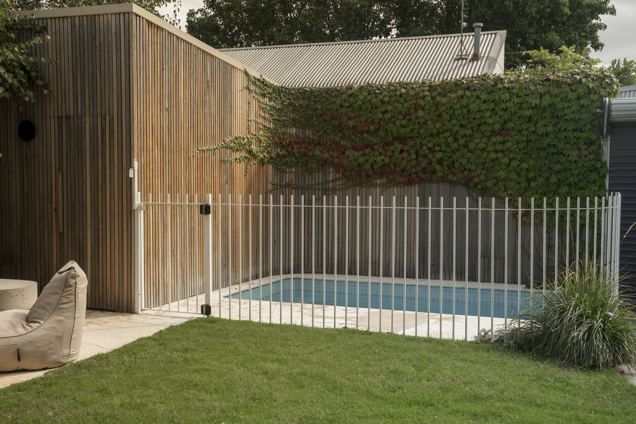 The tiled pool behind its white fence, timber clad shed on one side