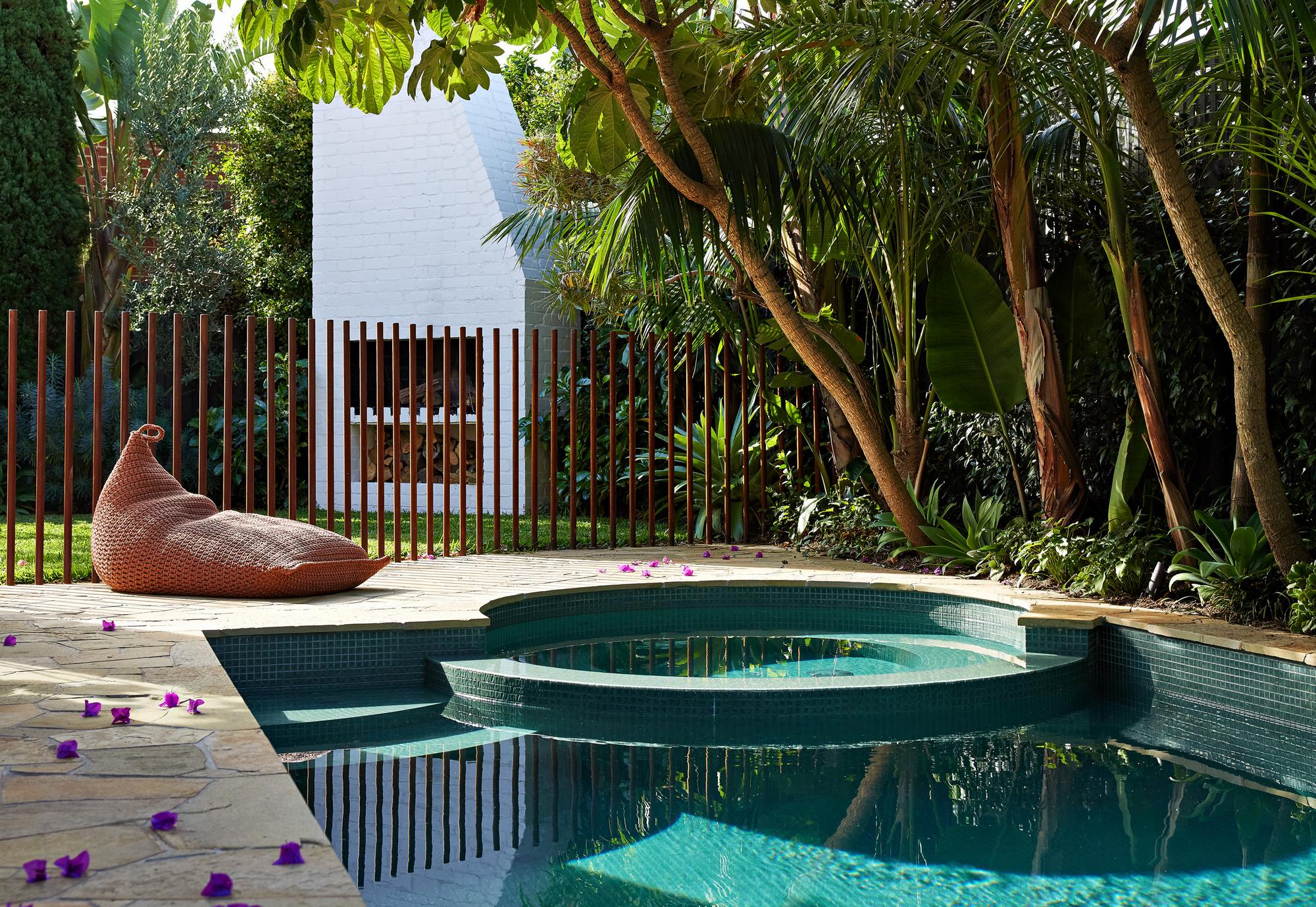 Tiled pool and round spa with a woven bean bag on the paving and the white brick fireplace beyond