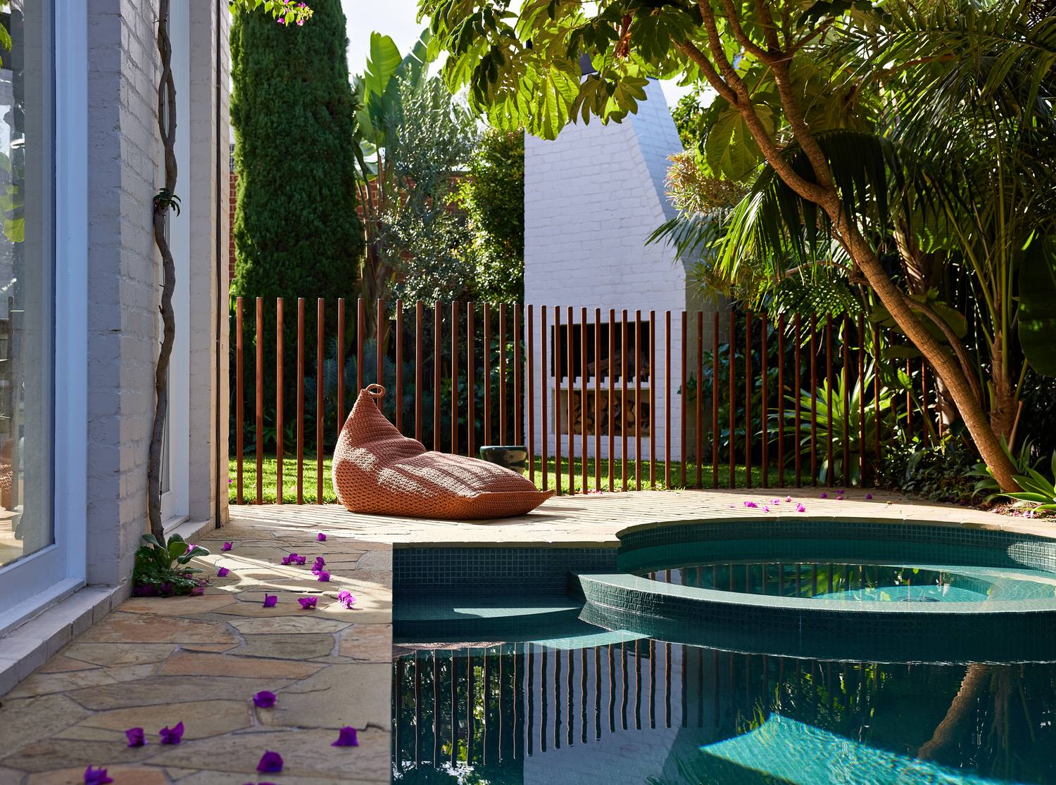 The pool and spa from the house windows, bougainvillea flowers across the paving