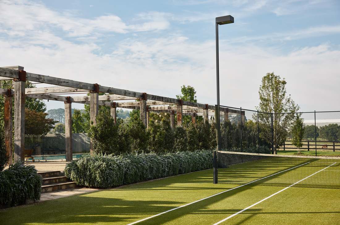 Tennis court edged with low planting, the pergola and pool beyond