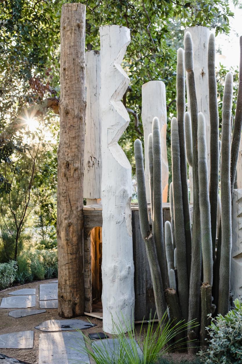 Carved and limewashed timber poles standing with tall cactus beside a recycled timber wall