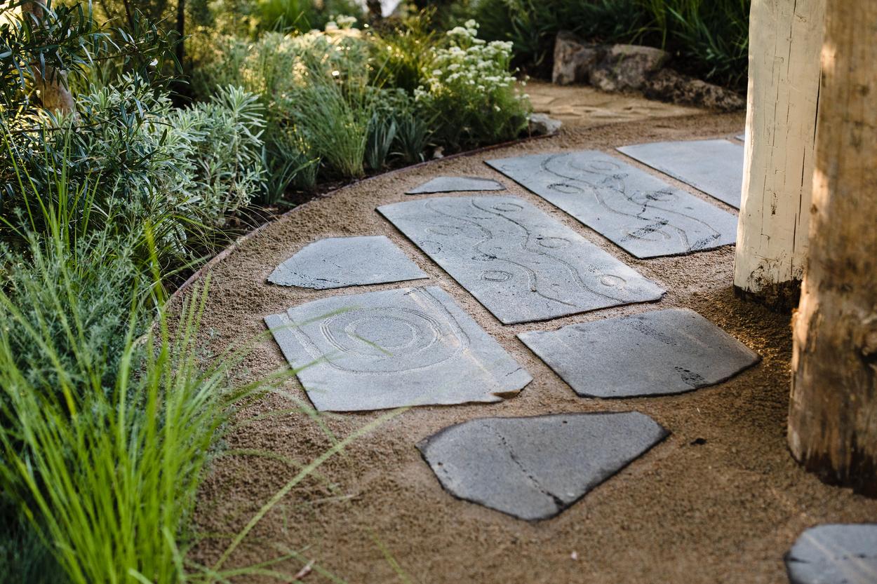 Bluestone stepping pavers hand etched with looping lines, set into the granitic sand
