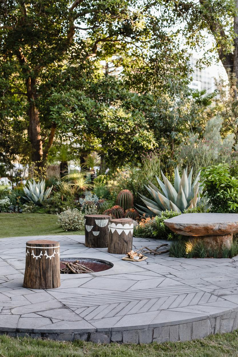 Painted timber stools around the sunken fire pit, agave and barrel cactus beyond