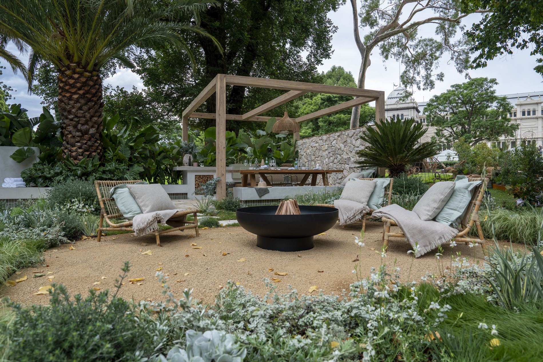 Fire pit and cane loungers on the gravel terrace, with the timber pergola and the Royal Exhibition Building beyond