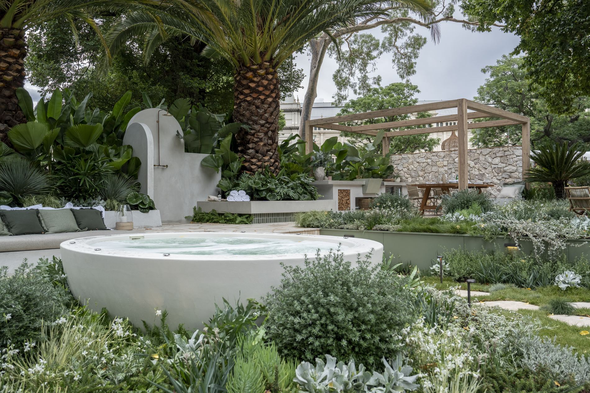 Round rendered spa set into silver planting, with the outdoor shower wall and pergola behind