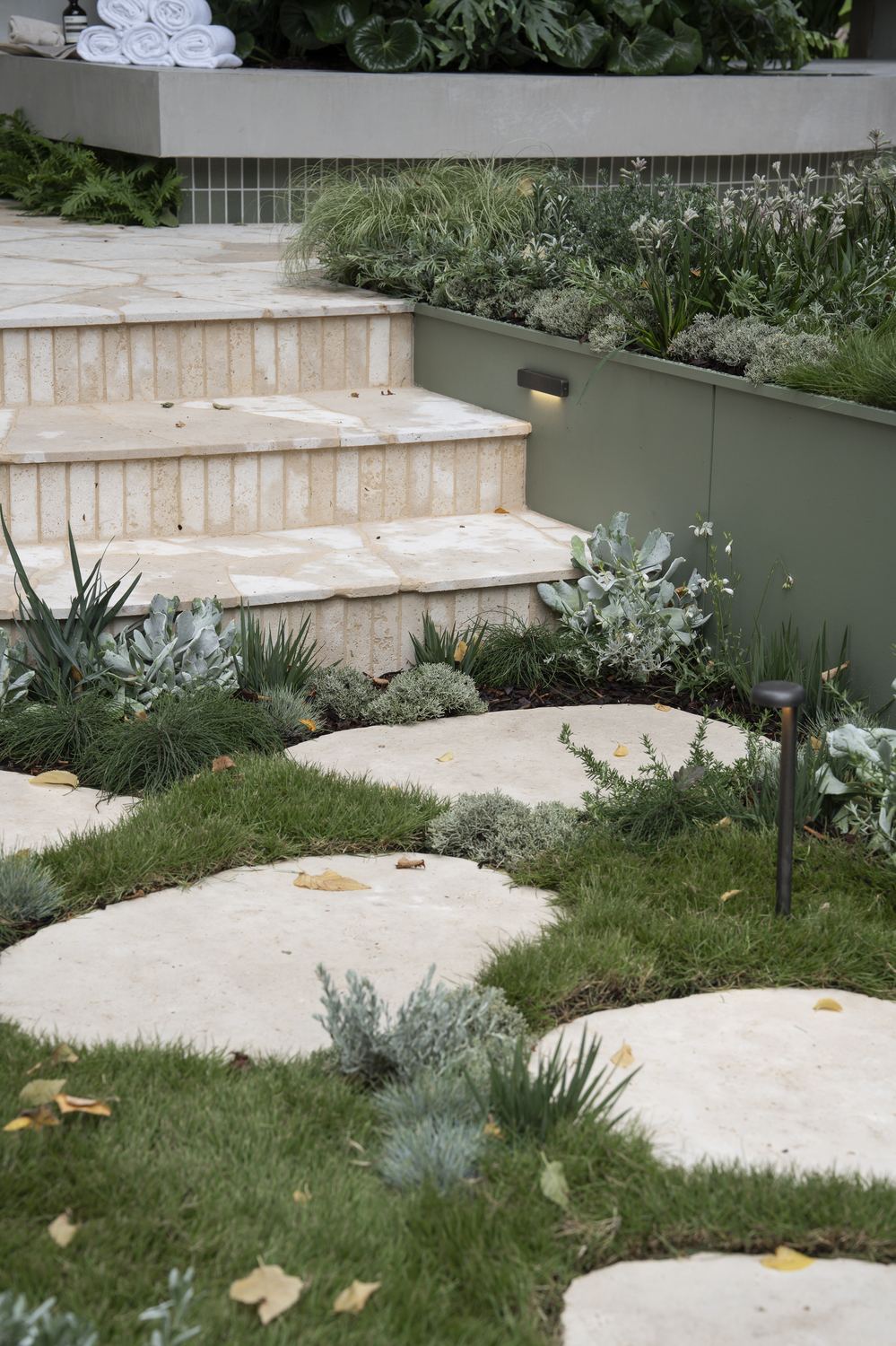 Fluted travertine step treads meeting the green steel planter edge and stepping stones