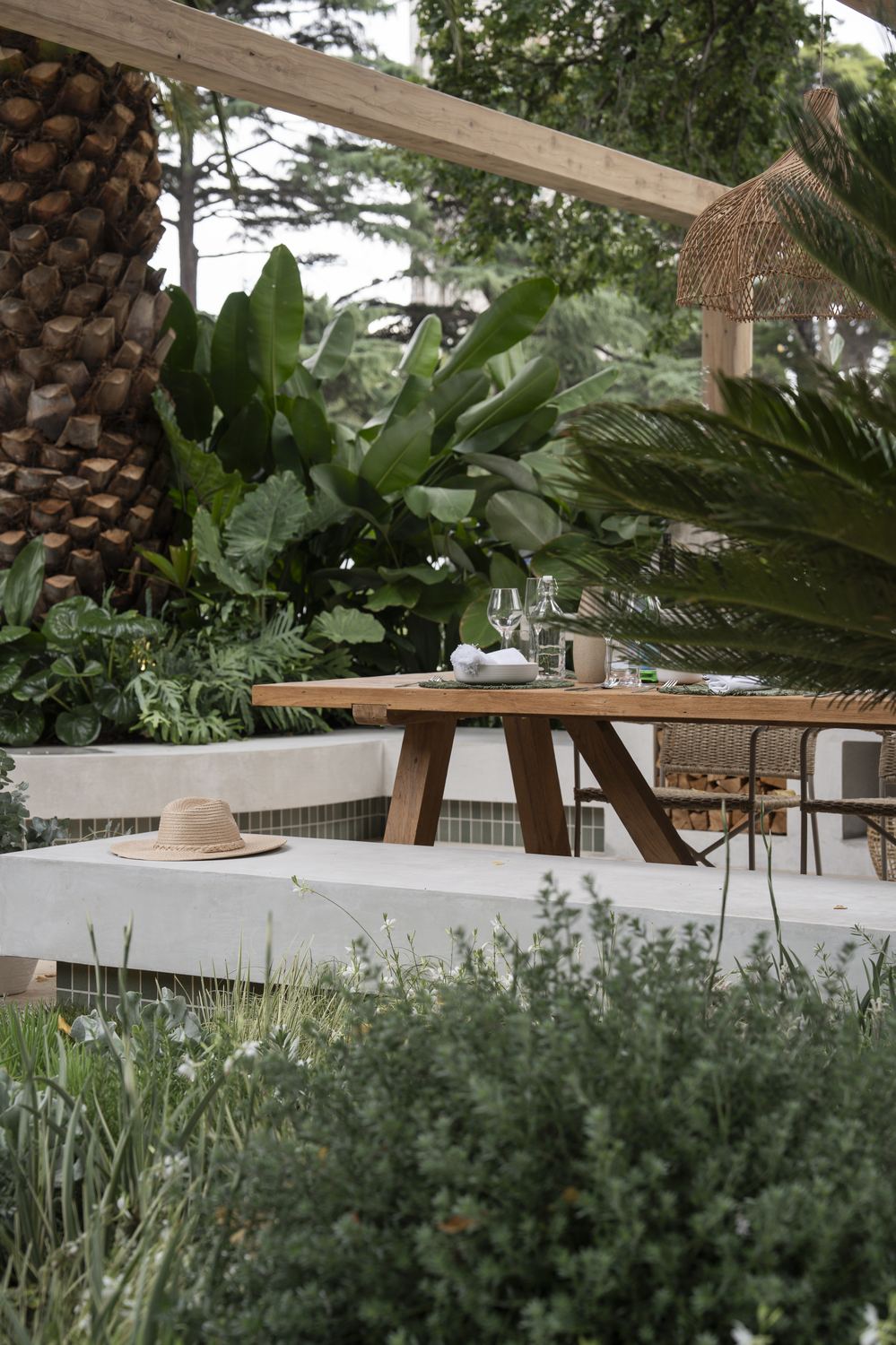 Timber dining table set under the pergola, rattan pendant above and a hat left on the bench