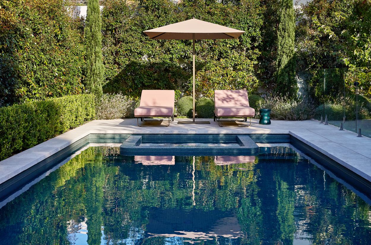 The pool and raised spa with two loungers and an umbrella on the stone surround, hedged and screened on every side